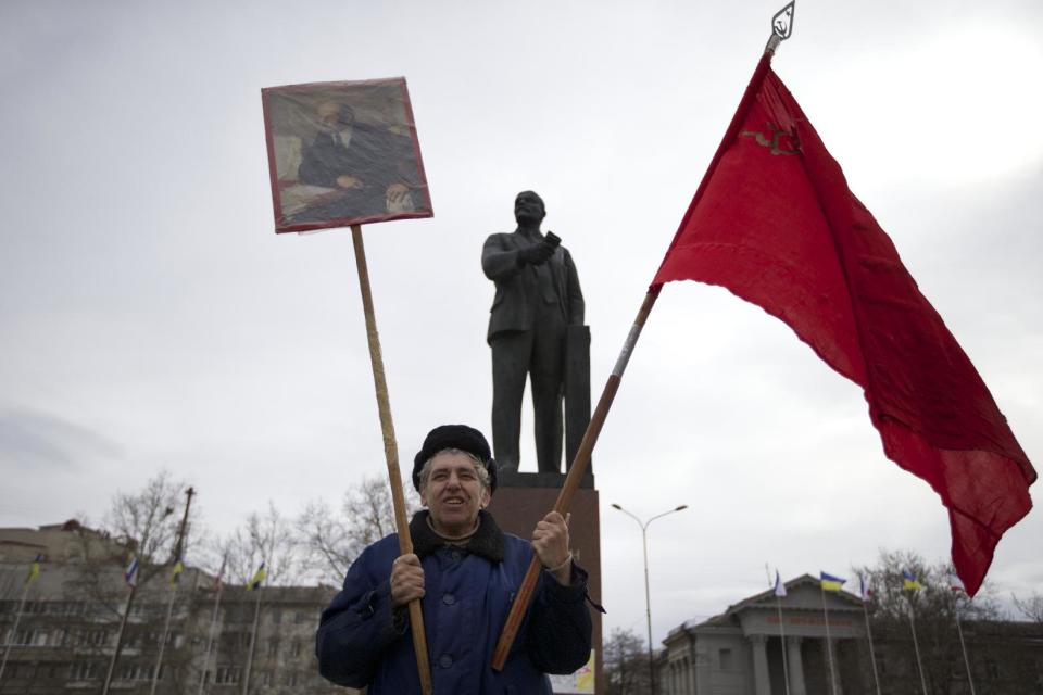 A local Communist party supporter holds Soviet flag and portrait of Soviet founder Vladimir Lenin as he stands next to Lenin's statue at a square in downtown Simferopol, Ukraine, on Sunday, March 2, 2014. A convoy of hundreds of Russian troops headed toward Simferopol the regional capital of Ukraine's Crimea region on Sunday, a day after Russia's forces took over the strategic Black Sea peninsula without firing a shot. (AP Photo/Ivan Sekretarev)