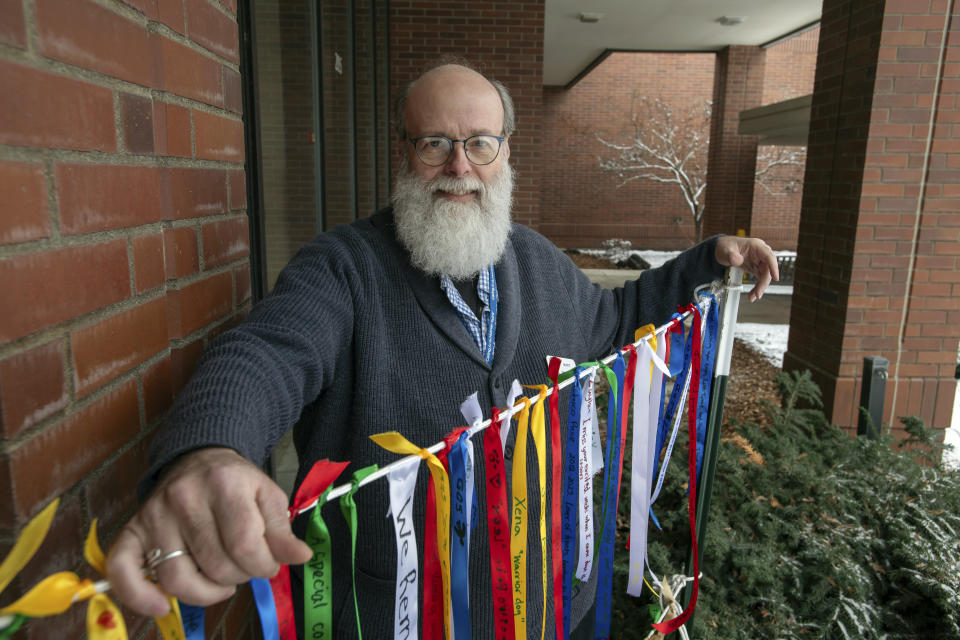 In this image provided by WSU College of Veterinary Medicine, Scott Campbell, the veterinary chaplain at Washington State University's College of Veterinary Medicine, poses for a photo outside the Veterinary Teaching Hospital in Pullman, Wash., Wednesday, Jan. 10, 2024. Next to Campbell is a string of ribbons from the "Garland Ceremony" he leads during "Celebration of Life & Remembrance" services held three times since the summer of 2023 that give community members a chance to come together for healing and grief. (Ted S. Warren/WSU College of Veterinary Medicine via AP)