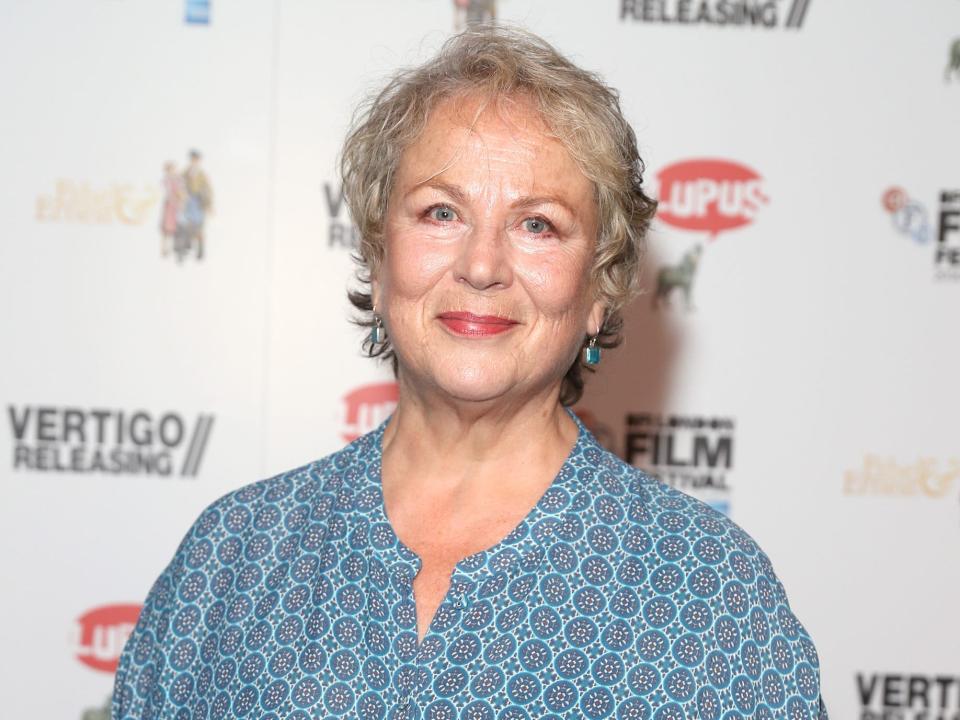 Pam Ferris in a loose blue and orange shirt in front of a white backdrop