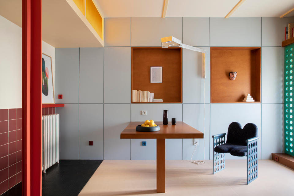 A dining area with wall-to-wall built-in cabinetry in pale blue, with a fold-down wooden table, red steel column and terracotta nooks