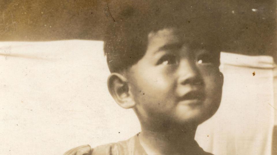 Michiko Kodama pictured as a small child in a black and white photograph. She is not looking at the camera, but looking up at someone with a happy expression on her face.