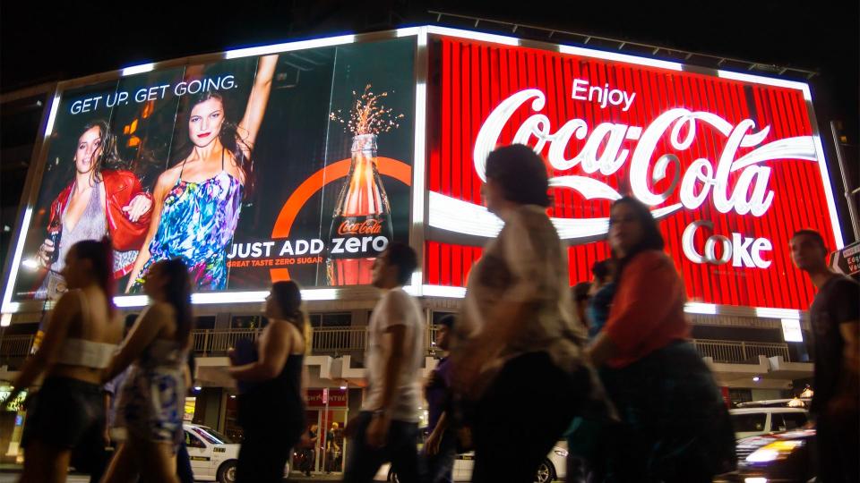 Sydney, Australia - March 22, 2014: A large group of people walk past two large neon Coca-Cola billboards on Kings Cross at night.