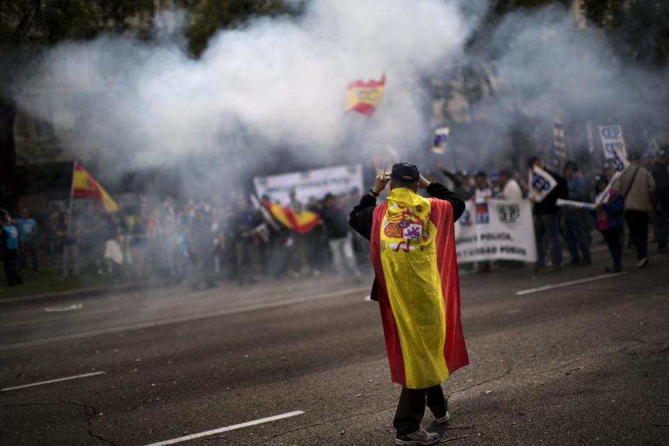 A police officer wearing an Spanish flag walks in front of a demonstration where other police officers protest as they block the street and light firecrackers next to the Interior Ministry in Madrid, Spain, Saturday, Oct. 27, 2012. The demonstrators were protesting parts of the austerity package, namely the elimination of one of 14 paychecks that most Spanish civil servants get each year. The one being axed comes right before Christmas. (AP Photo/Emilio Morenatti)