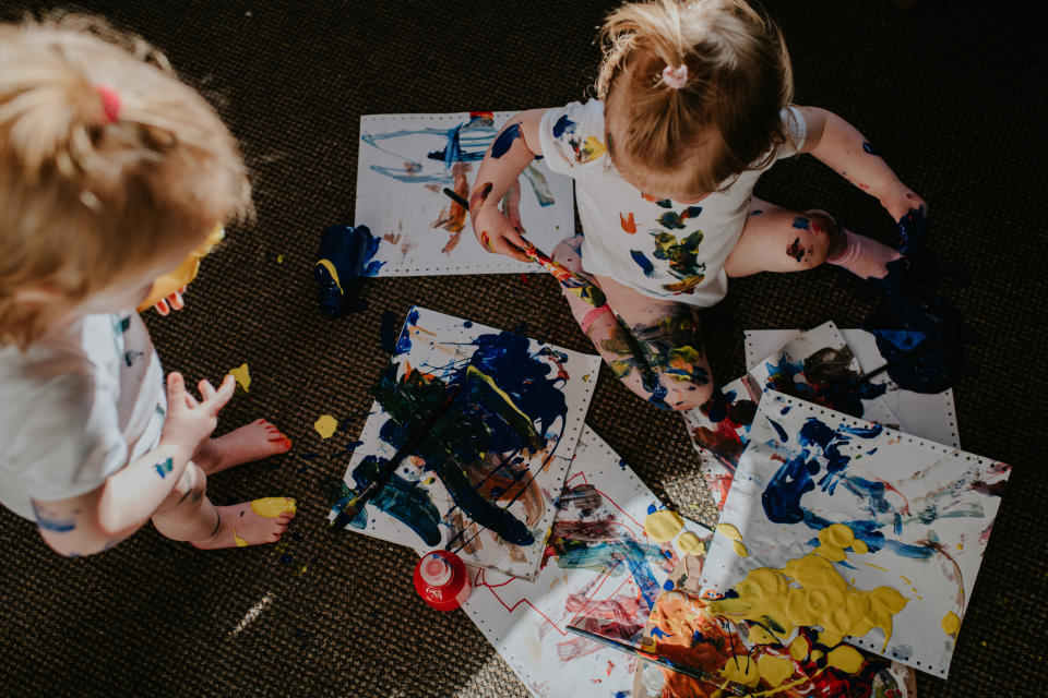 Two toddlers engaging in creative play with paint and paper on the floor