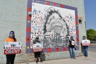 FILE - Activists hold signs promoting Native American participation in the U.S. census in front of a mural of Crow Tribe historian and Presidential Medal of Freedom recipient Joe Medicine Crow on the Crow Indian Reservation, Aug. 26, 2020, in Lodge Grass, Mont. A majority of tribal groups won't get the full suite of detailed demographic data from the 2020 census that they had in the previous census. Some of the available numbers are going to be imprecise because of new privacy safeguards recently implemented by the U.S. Census Bureau, according to a new report by the Center for Indian Country Development. (AP Photo/Matthew Brown, File)