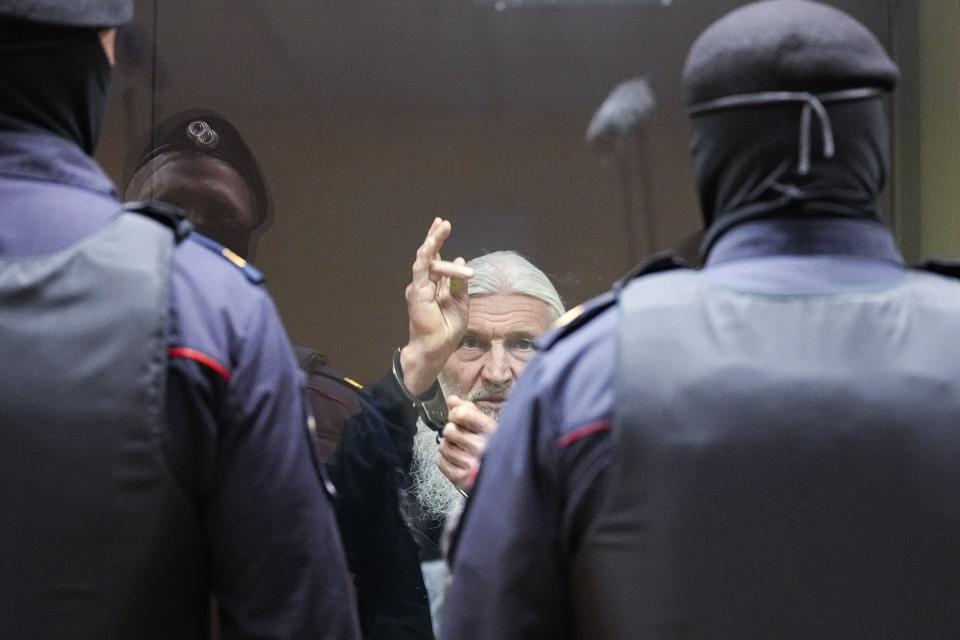 Nikolai Romanov, a former monk known as Father Sergiy until he was excommunicated by the Russian Orthodox Church, baptizes those present in the hall from behind a glass cage during his trial in Moscow, Russia, Friday, Jan. 27, 2023. The monk, who denied that the coronavirus existed and challenged the Kremlin, was handed a new prison sentence Friday on charges of inciting hatred. (AP Photo/Alexander Zemlianichenko)