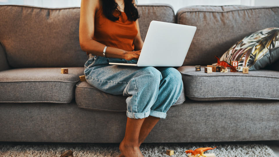 Cropped shot of a woman using a laptop on the sofa surrounded by toys at home.