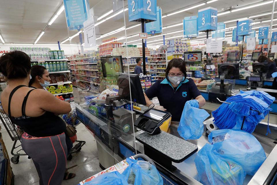 In this Wednesday, June 3, 2020 photo, cashier Rosario Vargas, center, bags groceries for customers at the Presidente Supermarket in the Little Havana neighborhood of Miami. The U.S. government is set to issue its latest report on the layoffs that have left millions unemployed but have steadily slowed as many businesses have begun to reopen and to rehire some laid-off workers. (AP Photo/Wilfredo Lee)