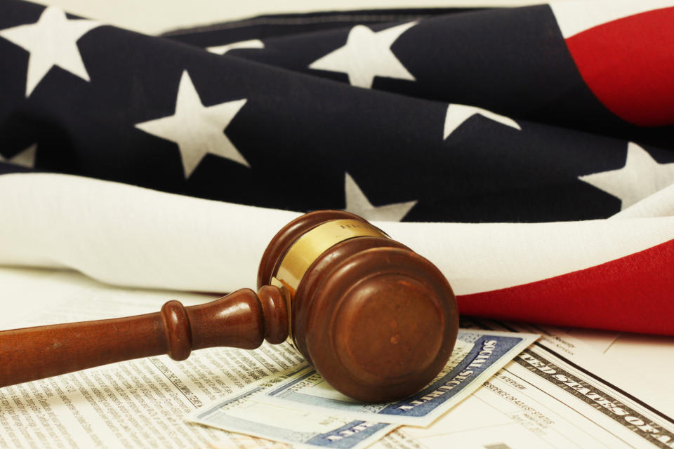 A judge's gavel lying atop two Social Security cards, with an American flag in the background.