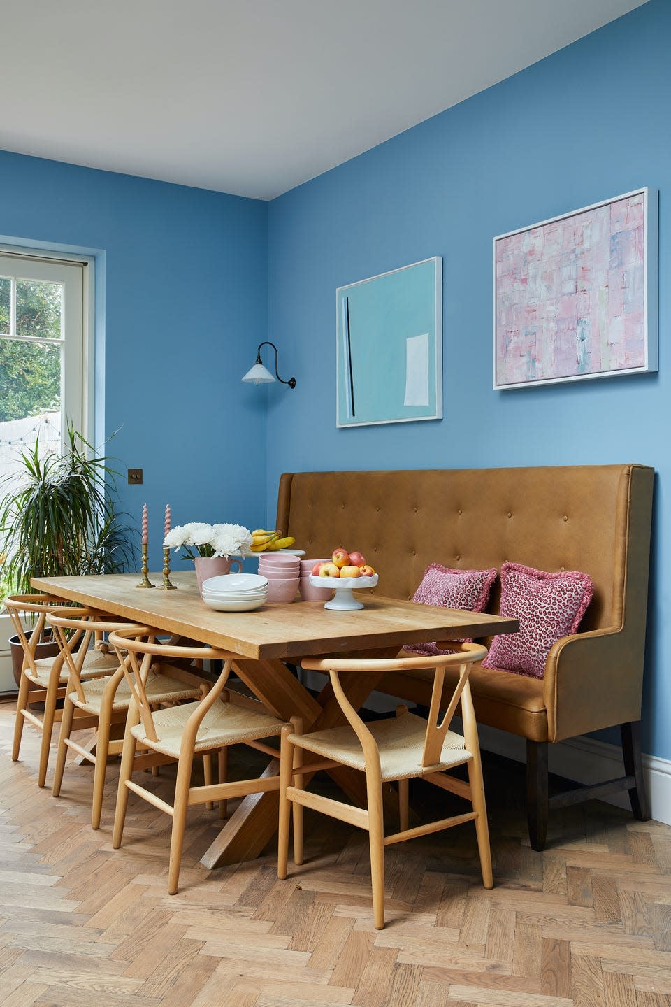 <p>Not only does a banquette reduce the footprint needed for chairs around a dining table, it can also be employed as a handsome piece of furniture in its own right.</p><p>'The expanse of wall this seat sits on is huge, so I designed this as a statement piece to really be a focal point,' explains interior designer Laura Stephens. 'The high back, slim side profile and tan leather complement the Hans Wegner Wishbone chair and pop against the lively blue painted wall.'</p><p>Pictured: A room from a project by <a href="https://www.laurastephens.co.uk/" rel="nofollow noopener" target="_blank" data-ylk="slk:Laura Stephens;elm:context_link;itc:0;sec:content-canvas" class="link ">Laura Stephens </a></p>