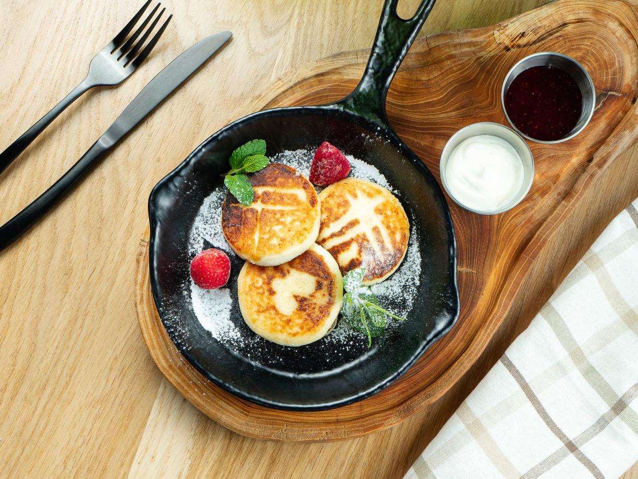 Traditional Ukrainian syrniki. Pancakes with cottage cheese in a pan with sour cream and jam on a wooden board. Top view, flat lay food