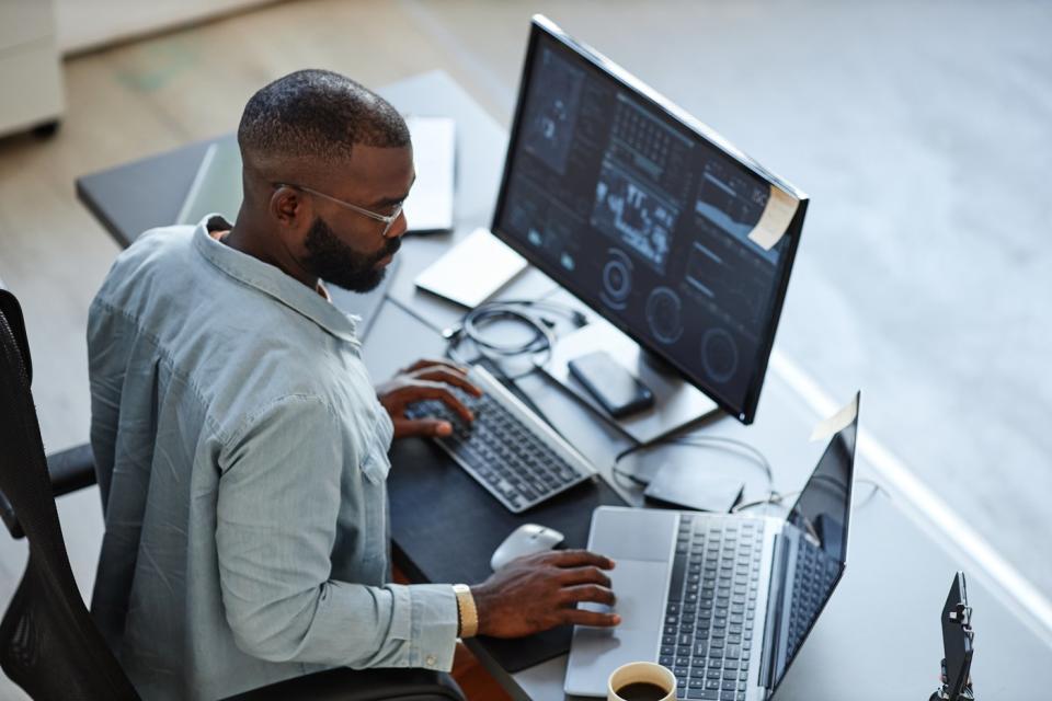 A person reviews financial information while sitting in front of multiple computer monitors.