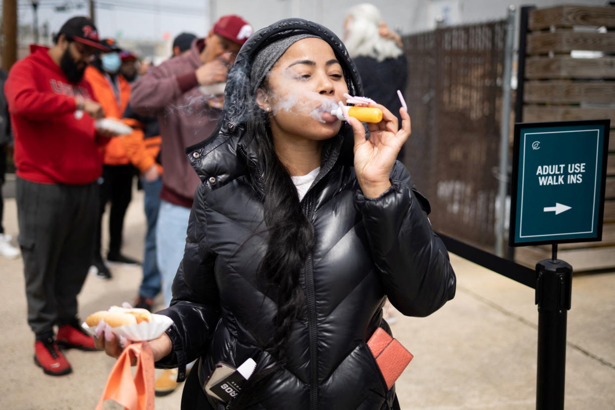 A customer smokes as she poses for a picture waiting in line to purchase marijuana products at Curaleaf as New Jersey launches recreational marijuana sales following voter approval in Bellmawr, New Jersey, U.S., April 21, 2022.  REUTERS/Hannah Beier