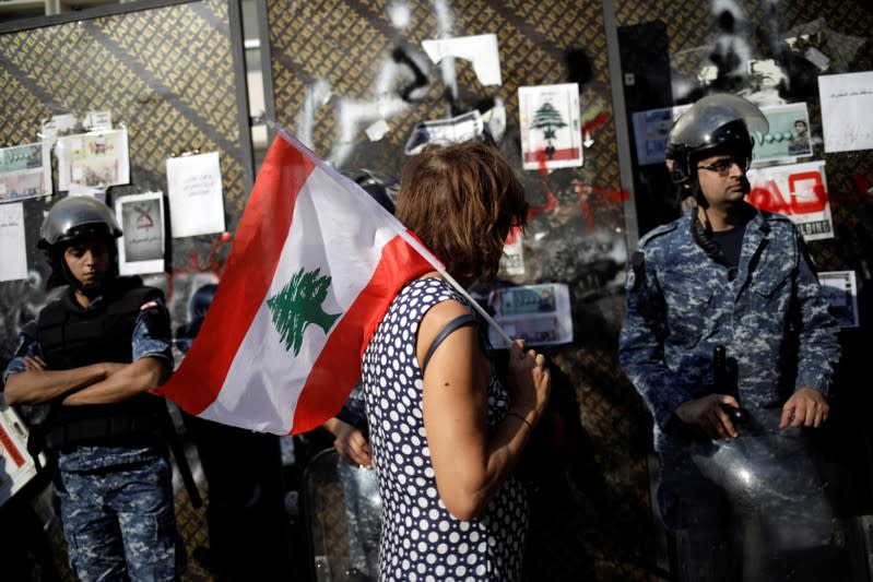 A protester holds a Lebanese flag as she walks in front of police officers stand guarding the Lebanon Central Bank at a demonstration during ongoing anti-government protests in Beirut