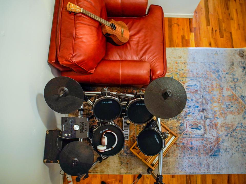 An aerial view of the author's music room shows wood floors, a grey rug, an electric drum kit, a red leather chair with a ukulele on it