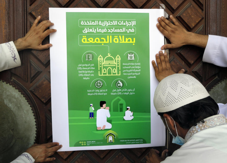 Workers place a poster with Arabic reads, "the precautionary measures and instructions inside mosques for Friday prayers" at al-Mirabi Mosque in Jiddah, Saudi Arabia, Thursday, May 28, 2020. The Ministry of Islamic Affairs said mosques will open to the public for prayers from May 31 until June 20, except in Mecca, with precautionary measures and instructions. (AP Photo/Amr Nabil)