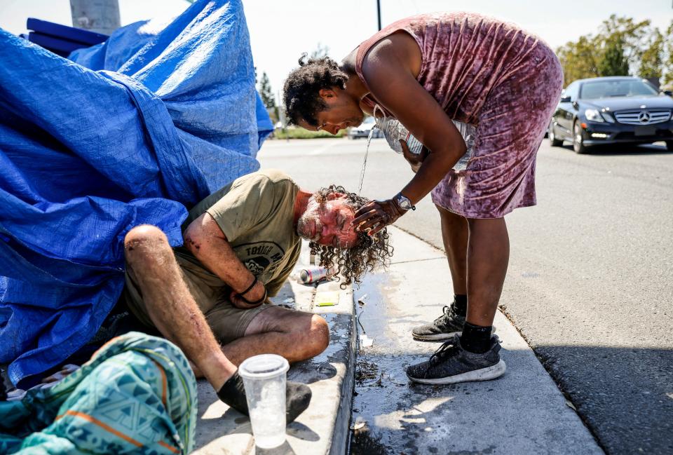 Angel Martinez pours water on Jerry Fullington's head to cool him off from the heat in Santa Rosa, Calif., on Wednesday, Sept. 7, 2022. The friends who used to be a couple have been homeless on and off for years but are hoping to get inside soon.