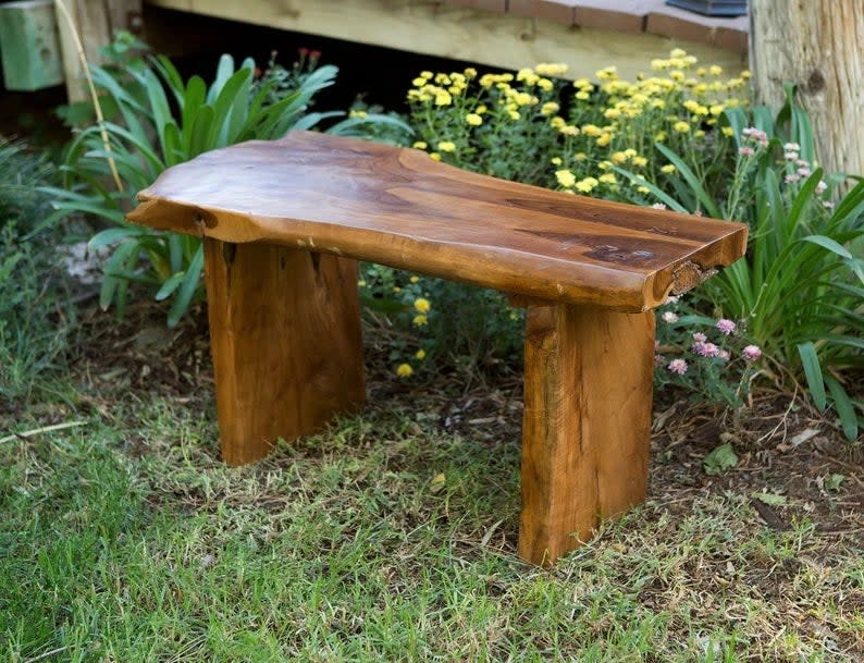 A teak garden bench surrounded by garden flowers. 