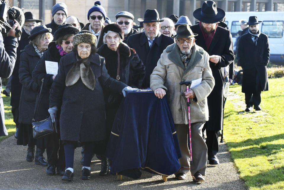 A group of Holocaust survivors transport a covered coffin with the remains of six unidentified Holocaust victims to be buried at the United Synagogue's New Cemetery in Bushey, England, Sunday Jan. 20, 2019. The remains of six unidentified Holocaust victims have been buried at a Jewish cemetery after spending years in storage at a British museum. The Imperial War Museum found the ashes and bone fragments during a stock-taking last year. Hundreds of mourners watched as the remains of five adults and a child were buried at a cemetery outside London, in a coffin with earth from Israel. (John Stillwell/PA via AP)