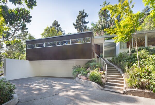 The preserved midcentury sits above its circular drive, surrounded by thick landscaping.