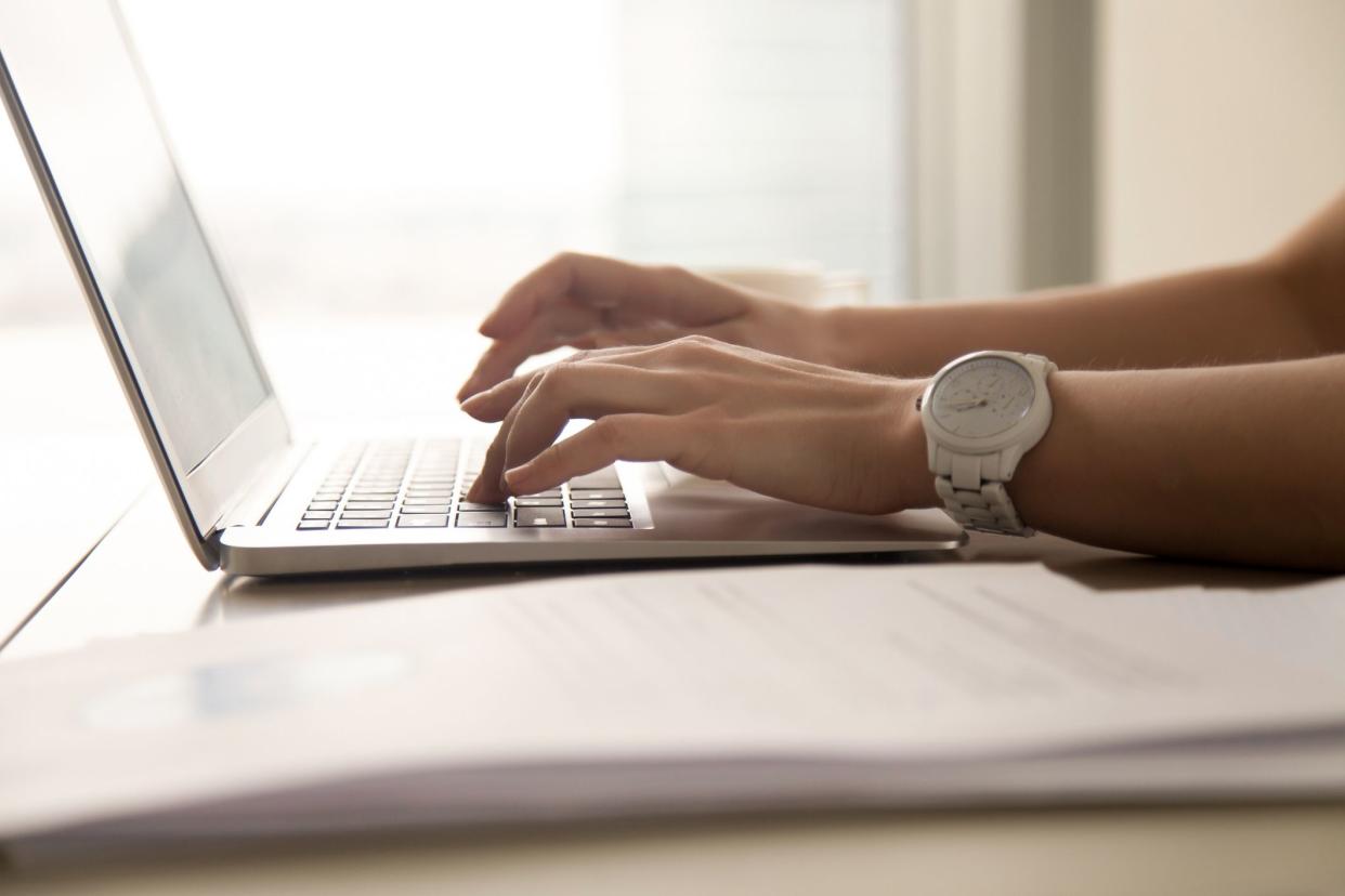 close-up of hands typing on laptop, papers on the side