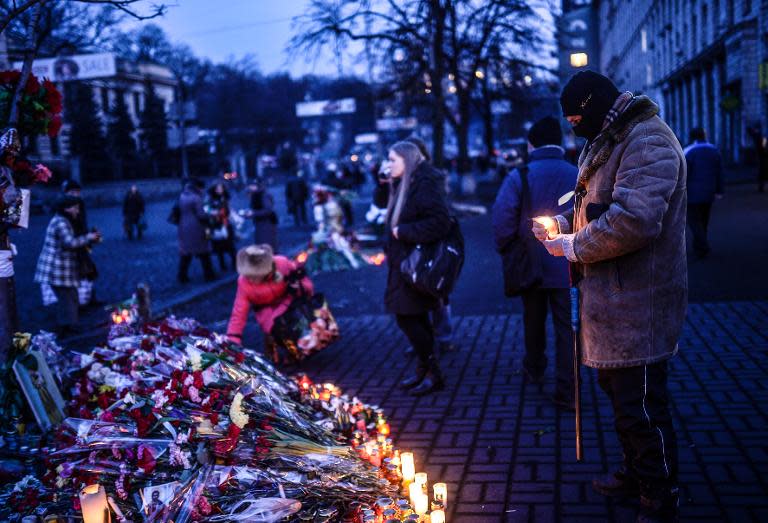 A man holds a candle as he stands near flowers laid in memory of anti-government protestor killed in clashes with police in central Kiev on February 26, 2014