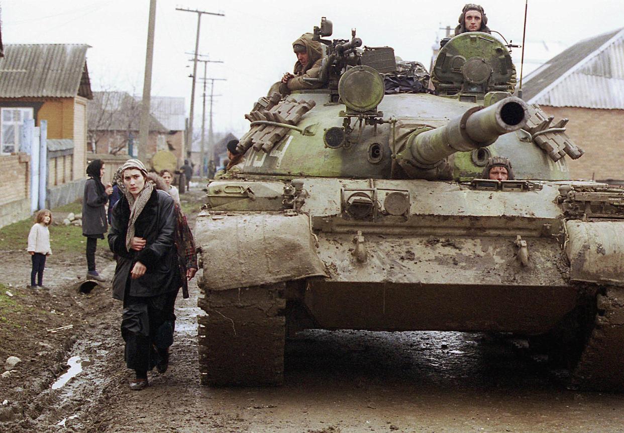 A Chechen woman passes by a tank of Russian federal troops on the main street of a village south of Grozny