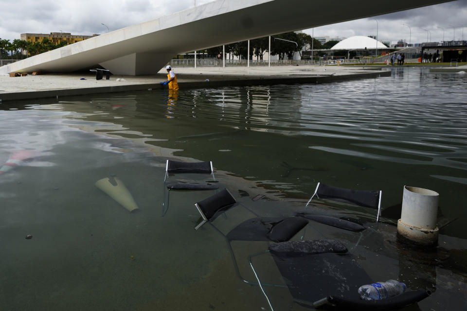 Furniture that was thrown from the ramp of Planalto Palace lay in the reflection pool where a worker collects them, the day after the office of the president was stormed by supporters of Brazil's former President Jair Bolsonaro in Brasilia, Brazil, Monday, Jan. 9, 2023. The protesters also stormed Congress and the Supreme Court. (AP Photo/Eraldo Peres)