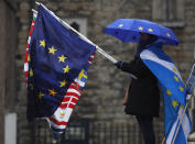 A pro EU protestor holds flags opposite the Houses of Parliament in London, Thursday, April 4, 2019. The British government and senior opposition figures were meeting Thursday in search of a new plan on how the country leaves the European Union as Prime Minister Theresa May tried to stop her shift toward compromise from splitting her Conservative Party. (AP Photo/Frank Augstein)