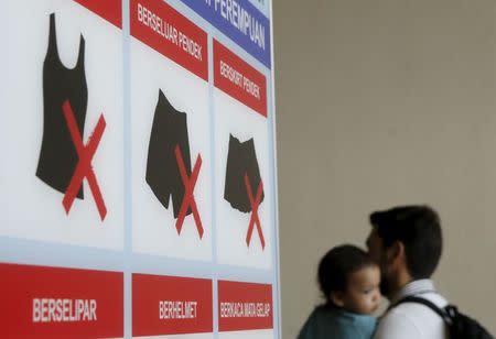 A man carrying a baby walks past a sign enforcing a dress code, outside a government building in Kuala Lumpur, Malaysia, July 15, 2015. REUTERS/Olivia Harris