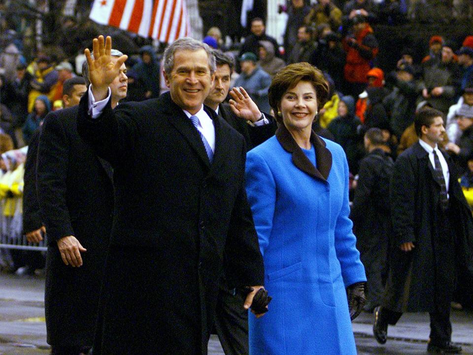 George and Laura in a bright blue and black lapel coat walking in the street.