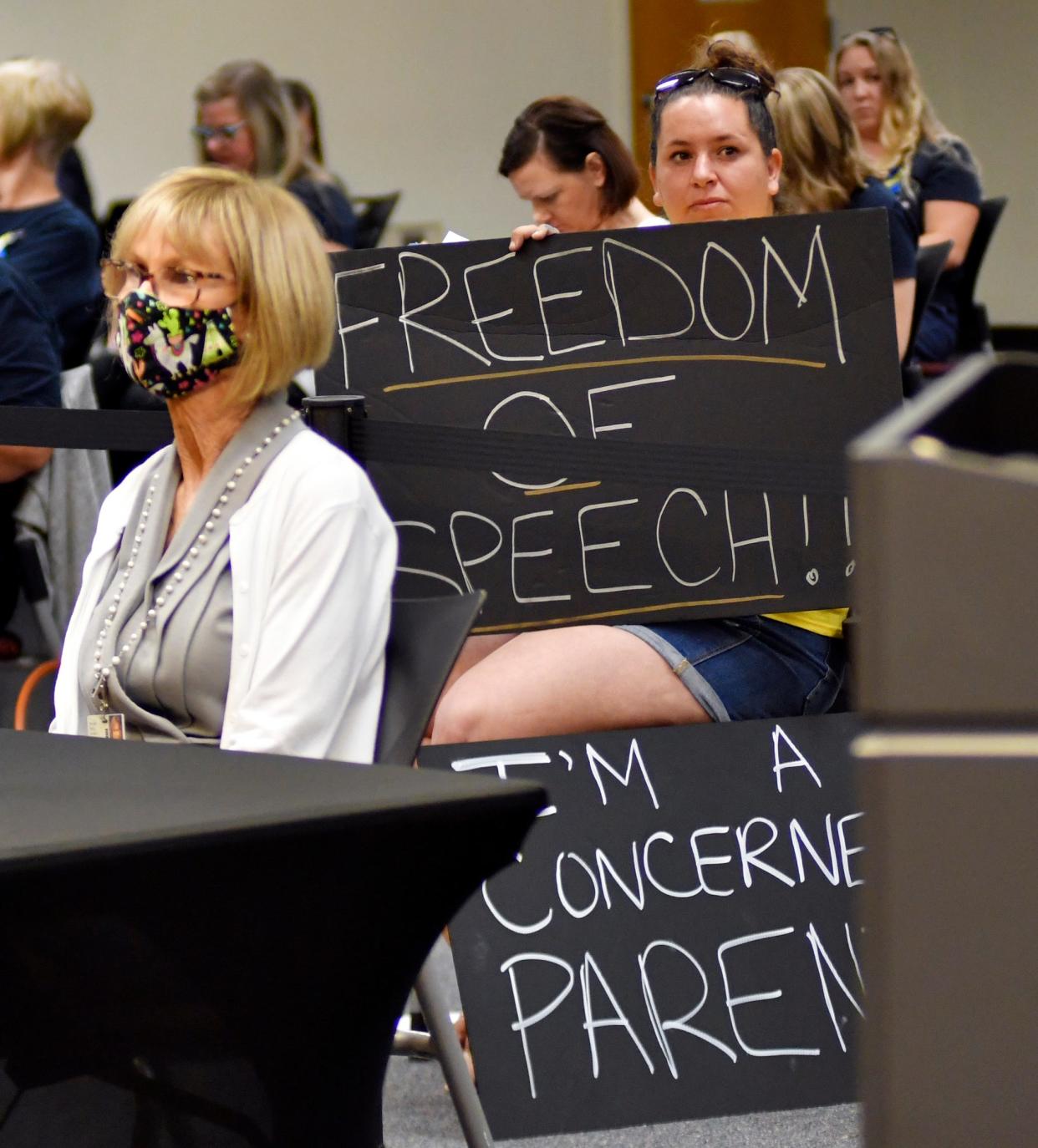 Katy Delaney, one of four parents who sued the School Board alongside the Brevard chapter of Moms for Liberty over the board's speaker rules, holds signs during an Oct. 26 School Board meeting.