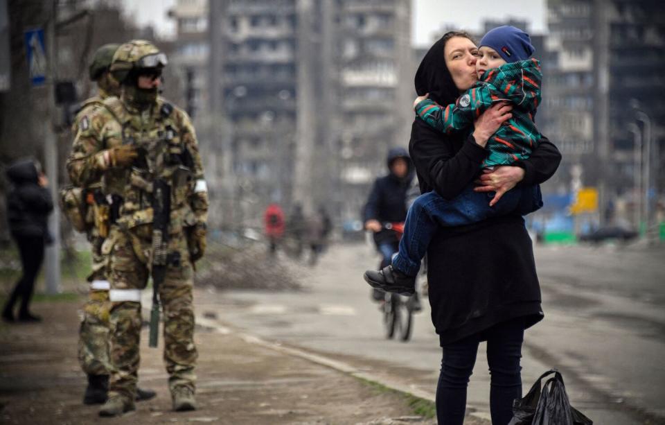 A woman holds and kisses a child while two soldiers near her.