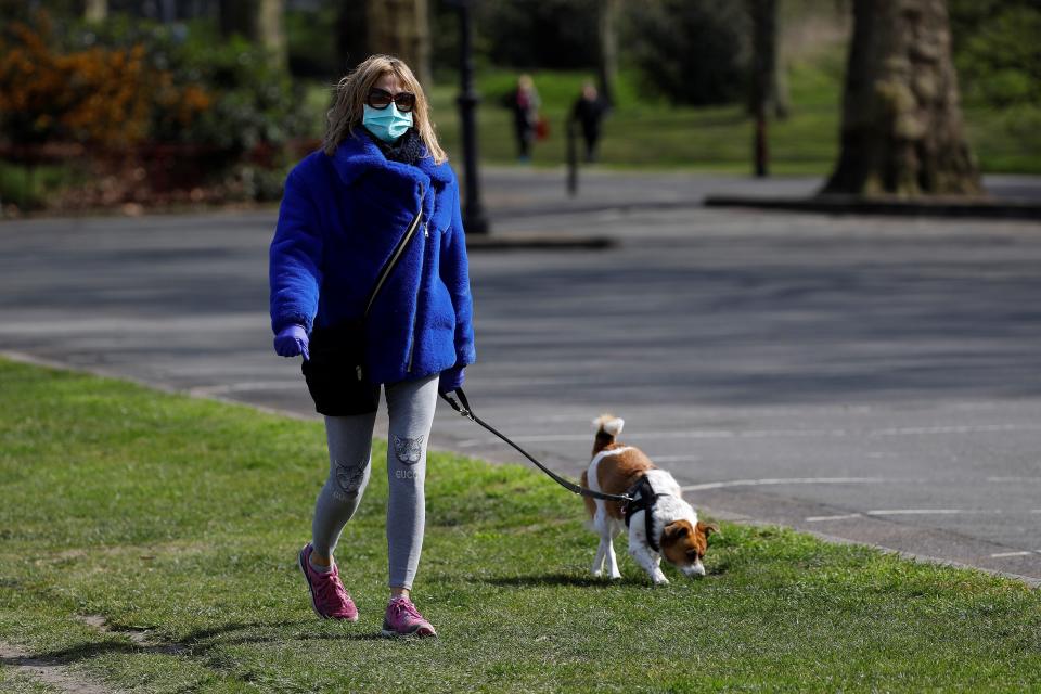 A woman wearing a face mask as a precautionary measure against Covi-19,=m=, walks a dog to get her exercise in Battersea Park in London on March 28, 2020, as life continues in Britain during the novel coronavirus pandemic. - The two men leading Britain's fight against the coronavirus -- Prime Minister Boris Johnson and his Health Secretary Matt Hancock -- both announced Friday they had tested positive for COVID-19, as infection rates accelerated and daily death rate rose sharply. (Photo by Tolga AKMEN / AFP) (Photo by TOLGA AKMEN/AFP via Getty Images)