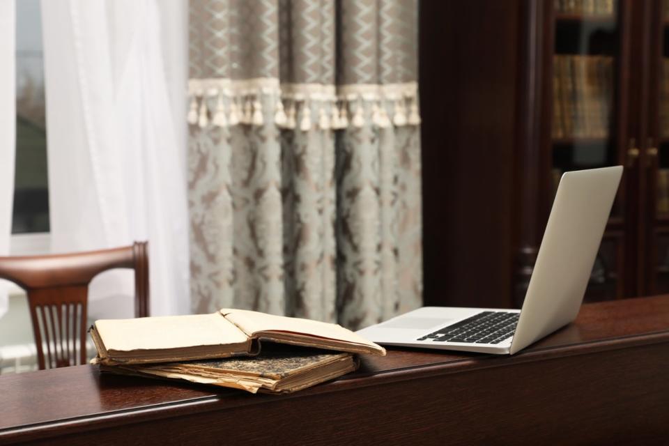 An-open-laptop-sits-on-a-wooden-ledge-along-with-vintage-books-and-antique-furnishings.