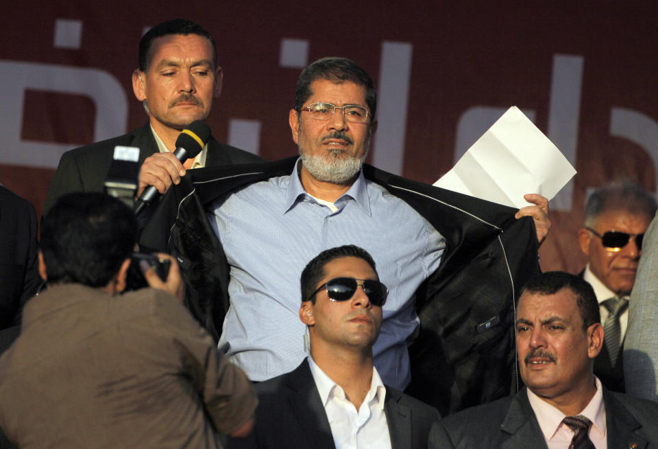 FILE - In this June 29, 2012 file photo, Egypt's President-elect Mohammed Morsi opens his suit jacket to show to his supporters that he is not wearing body armor at Tahrir Square, the focal point of Egyptian uprising, during his speech in Cairo, Egypt. Morsi’s collapse and death in a Cairo courtroom on June 17, 2019, was a brief rallying point for the Muslim Brotherhood whose influence waned dramatically in the Middle East since the 2013 military coup in Egypt which had widespread public support at the time. The long-running enmity between the Brotherhood and most Sunni-led governments highlights the deep divisions among Sunni Muslims. It adds a further complication to the volatile region, where the split between Sunnis and Shiite Muslims has created rival camps. (AP Photo/Amr Nabil, File)