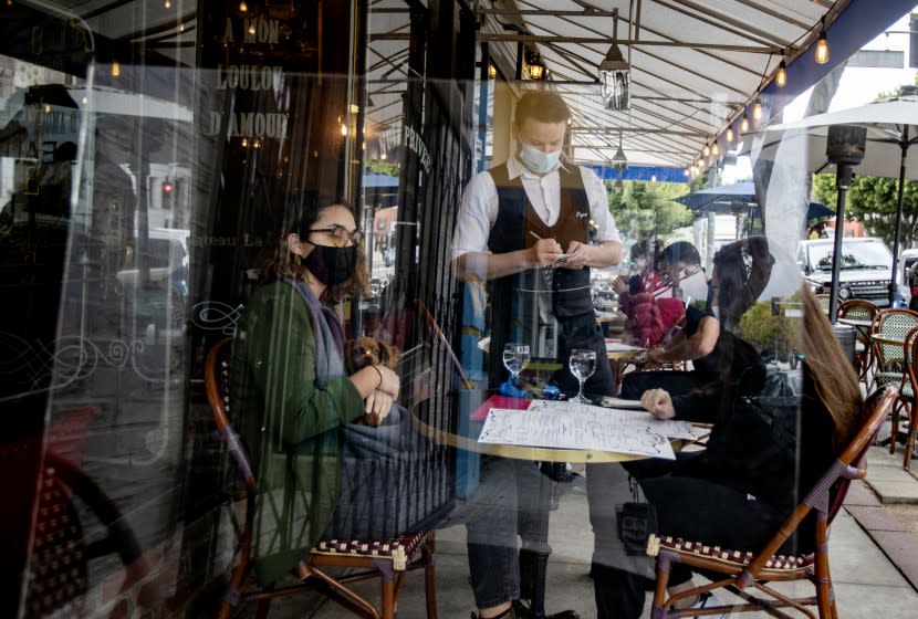 LOS ANGELES, CA - MARCH 15, 2021: Waiter Boris Macquin serves customers behind plexiglass outside at Figaro Bistro on the first day Los Angeles County allows indoor seating since the coronavirus pandemic on March 15, 2021 in Los Angeles, California. Many customers didn't realize indoor seating was allowed. The restaurant spread out the indoor seating and installed plexiglass at each table.(Gina Ferazzi / Los Angeles Times)