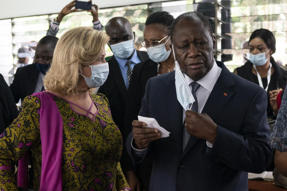 Ivory Coast President Alassane Ouattara removes his mask as he stands next to his wife Dominique Ouattara, left, after voting in a polling station during presidential elections in Abidjan, Ivory Coast, Saturday, Oct. 31, 2020. Tens of thousands of security forces deployed across Ivory Coast on Saturday as the leading opposition parties boycotted the election, calling President Ouattara's bid for a third term illegal. (AP Photo/Leo Correa)