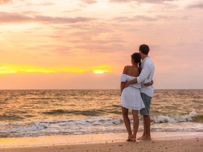 Couple with their back to camera watching the sunset as they hold each other