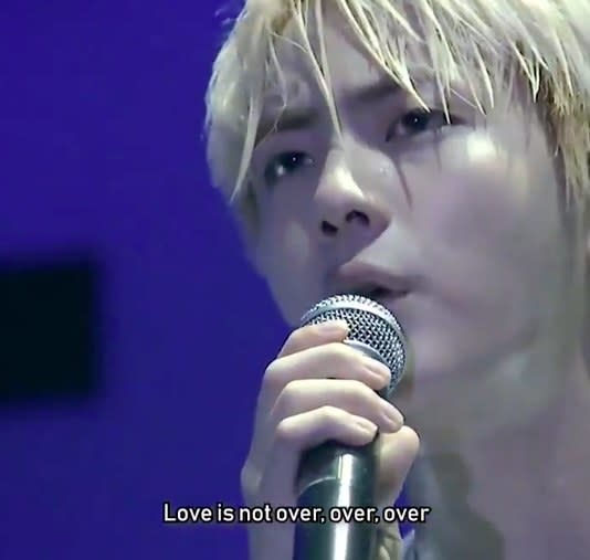 Close-up of Jin with bleached blond hair singing into a microphone with the caption "Love is not over, over, over"