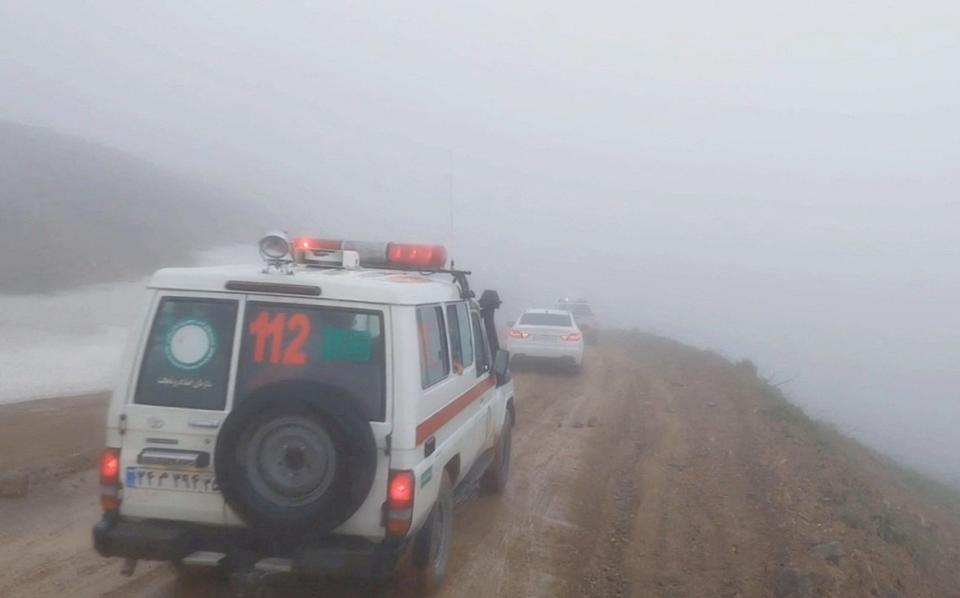 An ambulance and other vehicles drive on a foggy road as the search to find the crash site continues