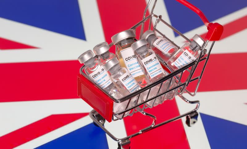 A small shopping basket filled with vials labeled "COVID-19 - Coronavirus Vaccine" is placed on a UK flag