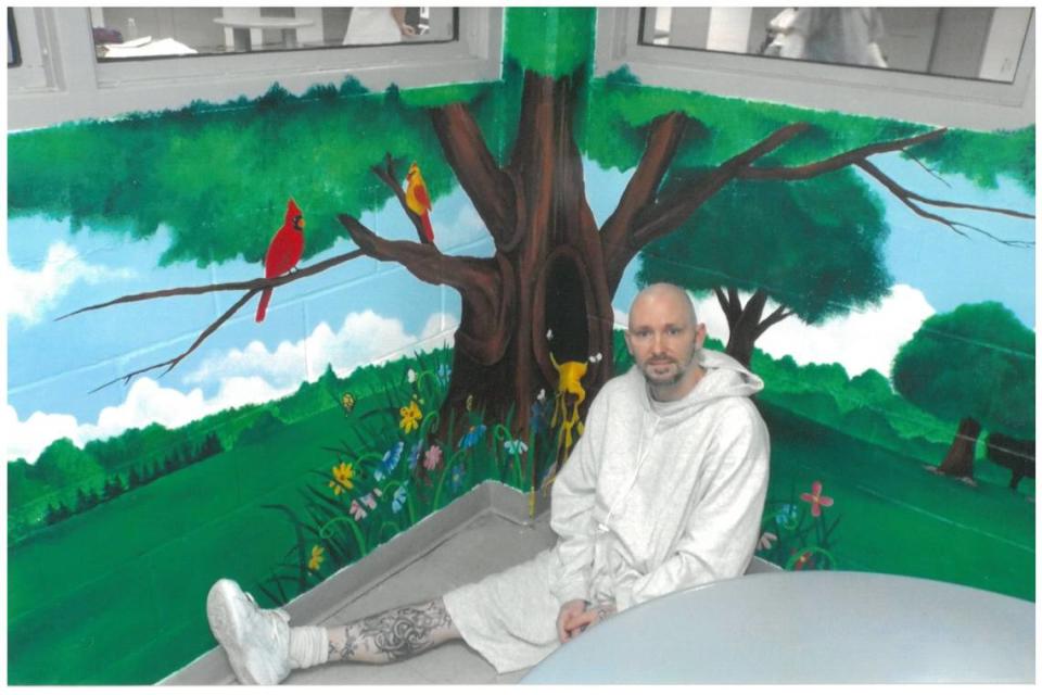 Michael Tisius sits by a mural he painted in a Missouri prison. The 42-year-old said art has been therapeutic for him.