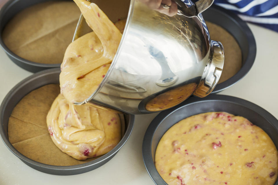 someone pouring cake batter with raspberries into separate cake pans