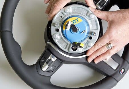 Le gonfleur de l'airbag d'un volant BMW, ici présenté retourné, pour montrer sa face arrière et ses branchements électriques. 