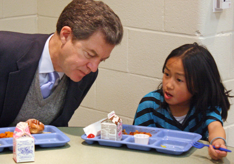 FILE - In this Jan. 23, 2014 file photo Kansas Gov. Sam Brownback, left, leans in to listen to Xen Hesse as the two each lunch at Roesland Elementary School in Roeland Park, Kan. On Friday, March 7, 2014, the Kansas Supreme Court said the state's current public school funding levels are unconstitutional. The case has broader implications beyond the classroom: Kansas enacted sweeping cuts to income taxes championed by Brownback that have reduced the amount of available resources to comply with a court order. (AP Photo/John Milburn, File)