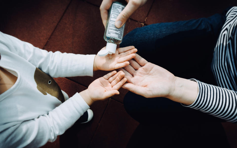 Overhead view of young mother squeezing hand sanitizer onto little daughter's hand in the playground to prevent the spread of viruses