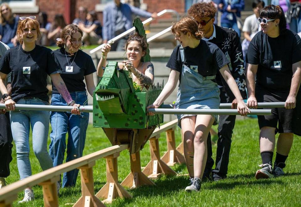 Sophomore illustration students aided Carly Burkholder, center, of Overland Park, who tossed dandelions as she rode her cardboard vehicle along the 80-foot wooden rail on Wednesday.