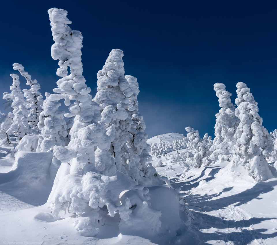 Long shadows fall across the frozen top of Indian Falls as morning light illuminates the MacIntyre Range in the Adirondack Park.