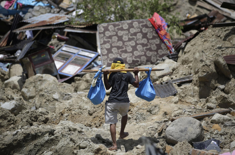 In this Oct. 6, 2018, file photo, a man carries belongings from his toppled house in the Balarola neighborhood of Palu city where a massive earthquake caused the soil to loosen like a liquid, swallowing some homes whole and collapsing others into piles of rubble in Central Sulawesi, Indonesia. (AP Photo/Aaron Favila, File)